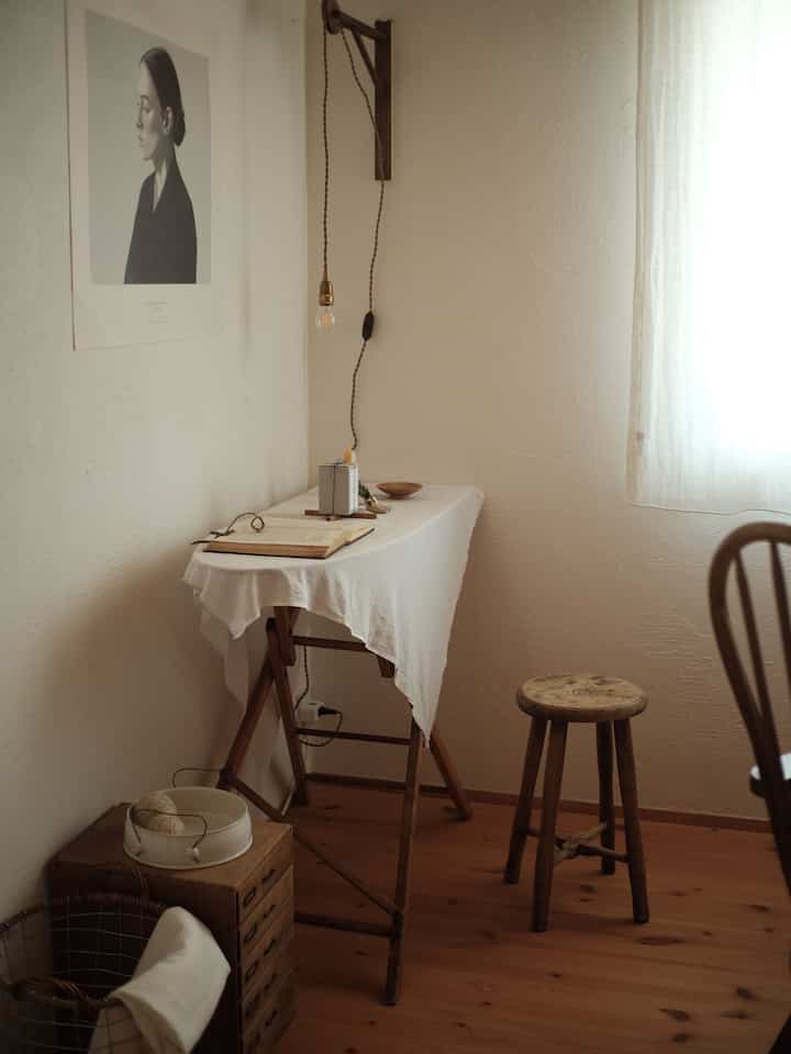 Small study with wood tones and white hues, featuring wooden desk and stool in a cozy setting