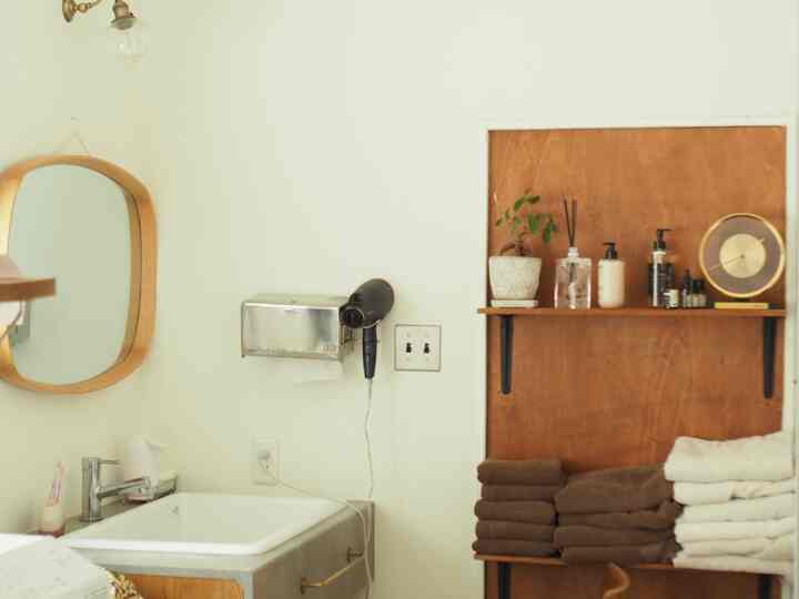 白い壁と木目調の棚が調和するバスルーム、整然としたタオルとミッドセンチュリーモダンの鏡が配置された印象的なパウダールーム