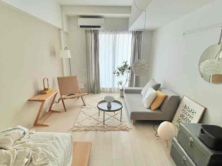 白とベージュの落ち着いた色調の小さなリビング、グレーのソファと木製のアームチェア、コーヒーテーブル、植物が配置された雰囲気のある空間