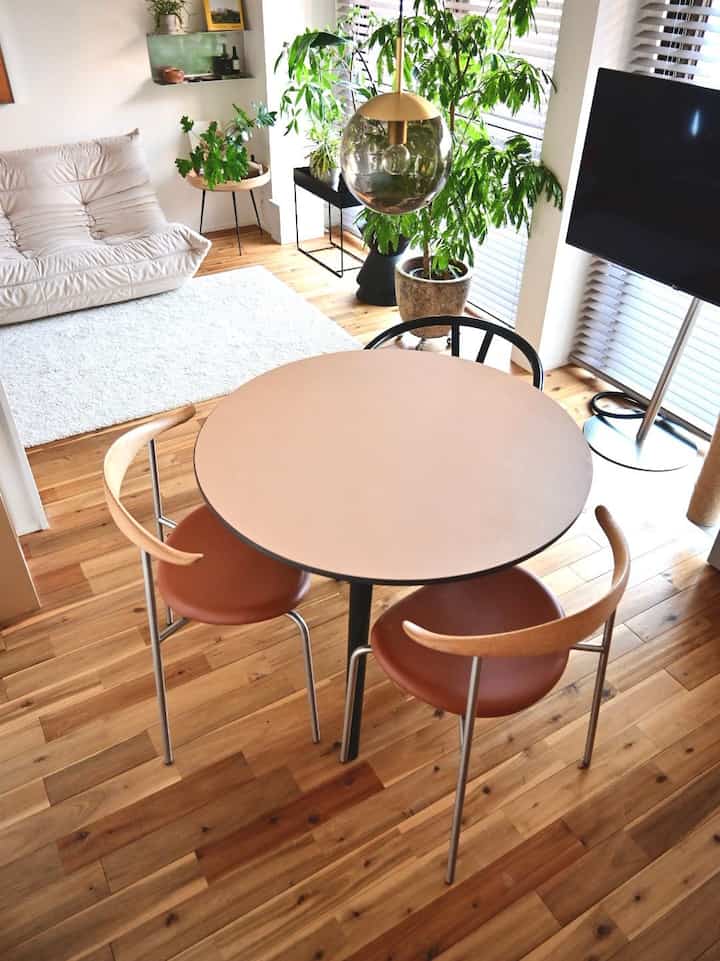 木目調の床と円形のダイニングテーブルが配置された自然な雰囲気のモダンダイニング、ソファと植物がある居心地の良い空間