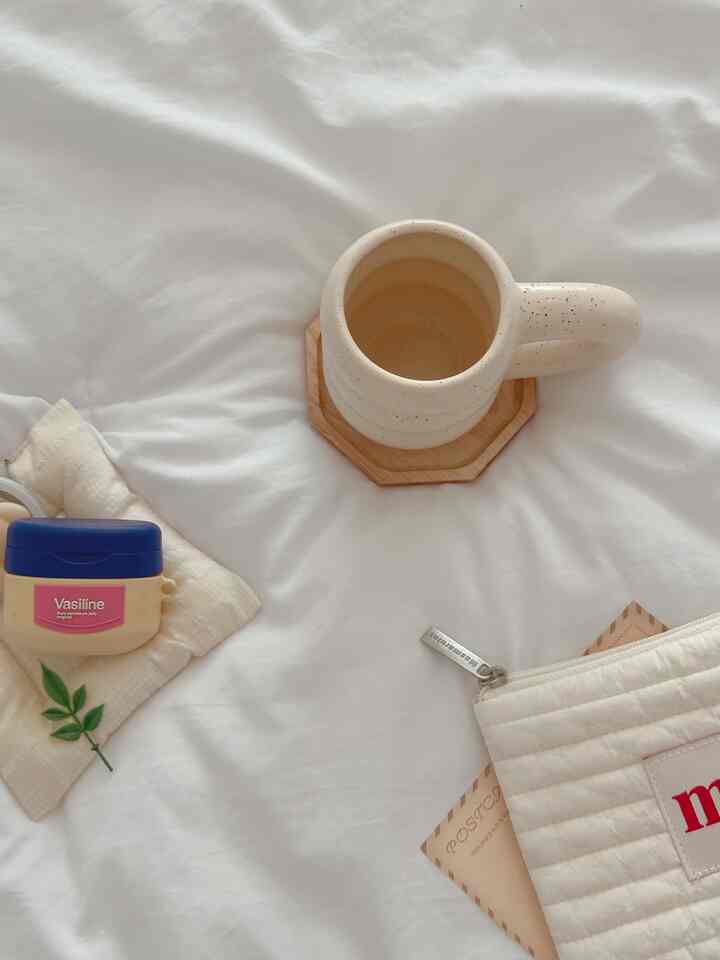 アイボリーの寝具の上にマグカップとワセリン、ポーチが配置されたミニマルな寝室の雰囲気のあるインテリア