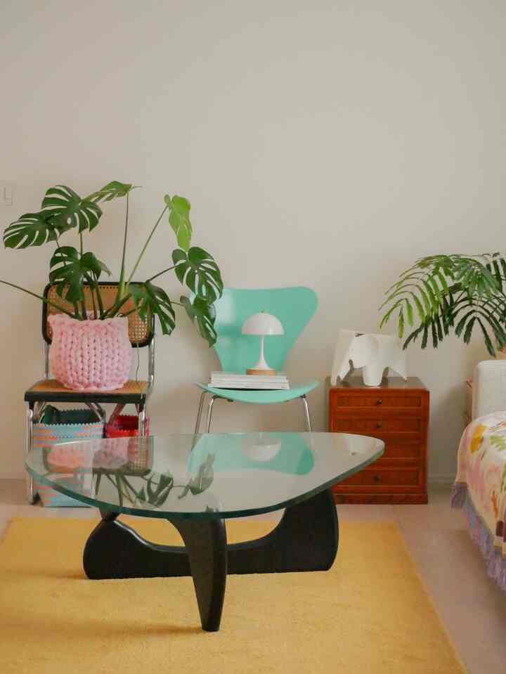 イエローカーペットとミント色のスツール、レトロスタイルの家具が配置された植物のある暖かいリビングルーム