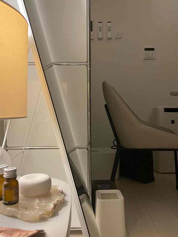 白とベージュの色調のダイニングルーム、ダイニングチェアとフレームなしの全身鏡が配置された印象的な空間