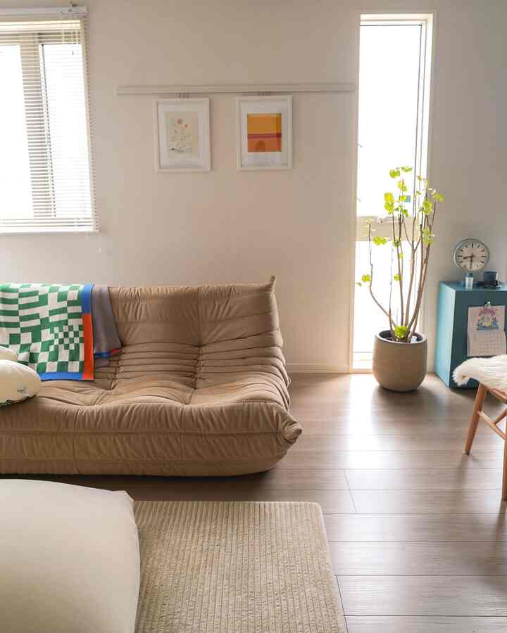 ベージュの落ち着いた色調のリビング、茶色のソファと緑の植物が配置された自然で心地よい空間