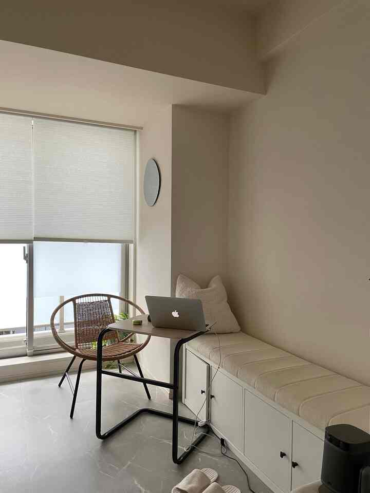 白とベージュの色調の狭いホームオフィス空間、ベンチとアームチェアが配置されたモダンなインテリア