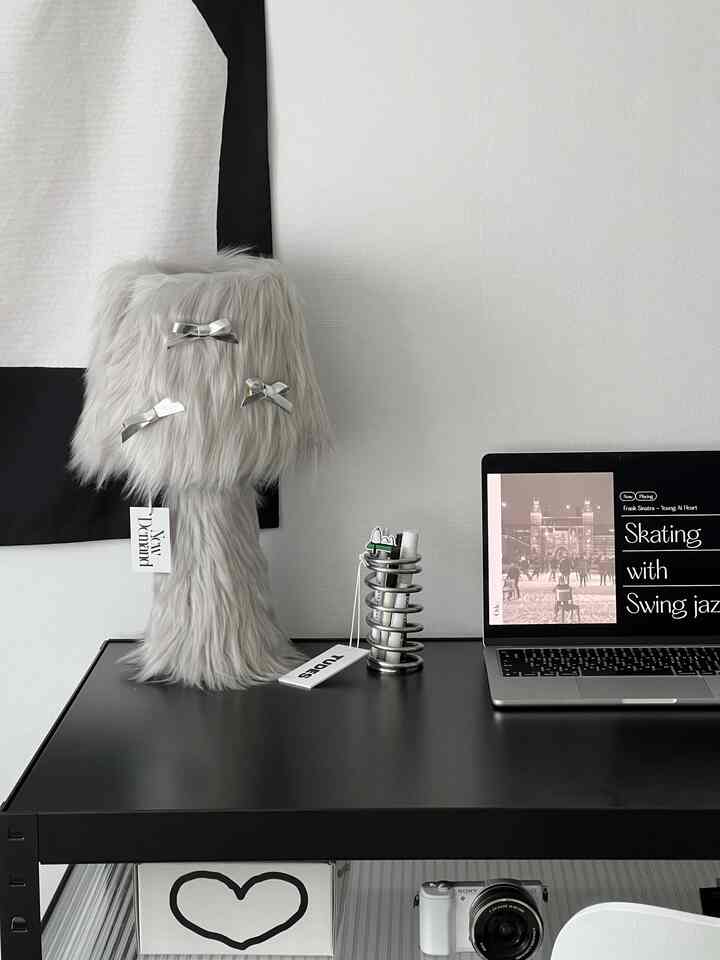 White and black tone home office space with a modern black desk featuring a gray furry lamp and an Apple MacBook laptop in a neat setup