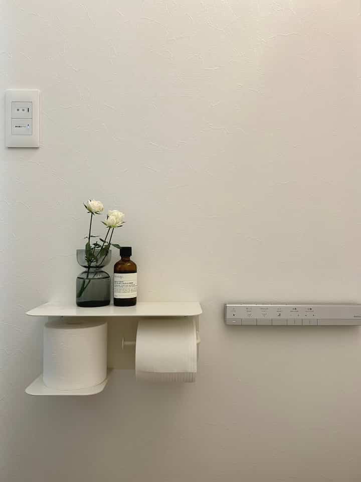 White-tone restroom wall featuring a simple paper holder and vase creating a clean, minimal space