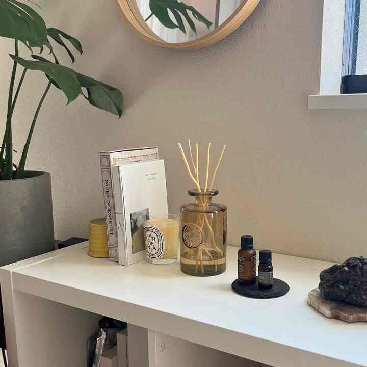 ナチュラルカラーの壁とホワイトの棚にキャンドル、ディフューザー、植物が配置されたシンプルで落ち着いたリビングのインテリア