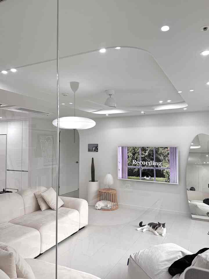 白とベージュのトーンのリビング、白いソファとビーンバッグ、テレビが配置されたミニマルで猫と暮らす雰囲気のあるインテリア