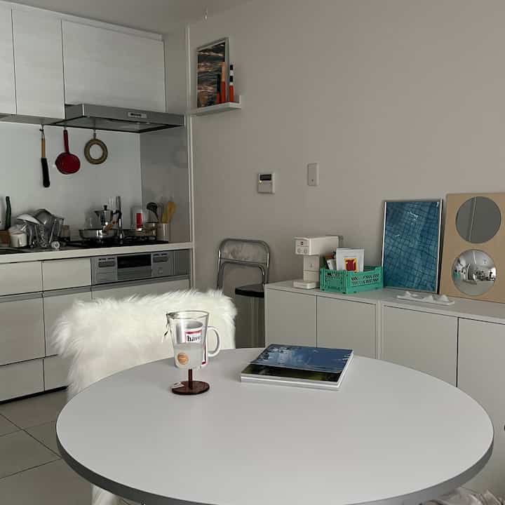 White-toned studio apartment kitchen and dining area featuring simple natural wood accents with a cozy atmosphere