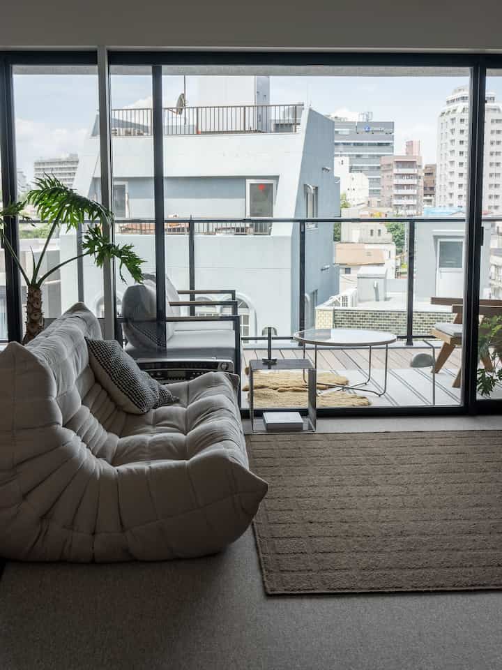 Natural-toned living room with beige sofa and carpet extending visually to a balcony featuring wood tones, creating a relaxed atmosphere