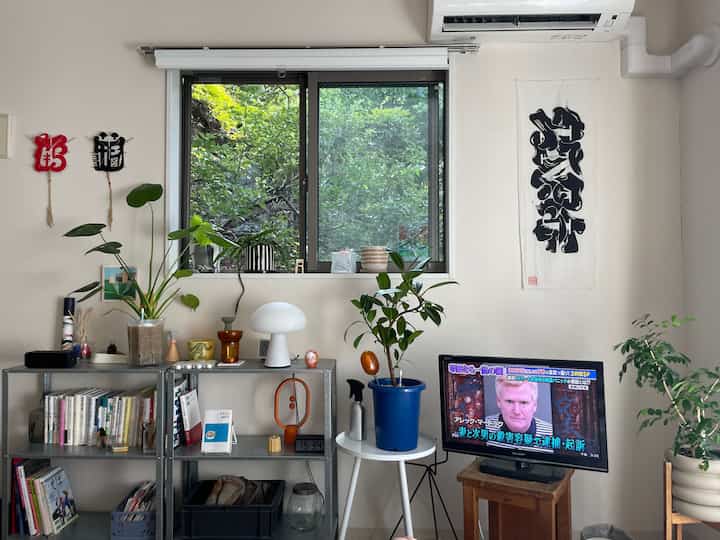 ナチュラルグリーンの色調のリビング、観葉植物とメタルの棚、テーブルランプが配置された落ち着いた印象の空間