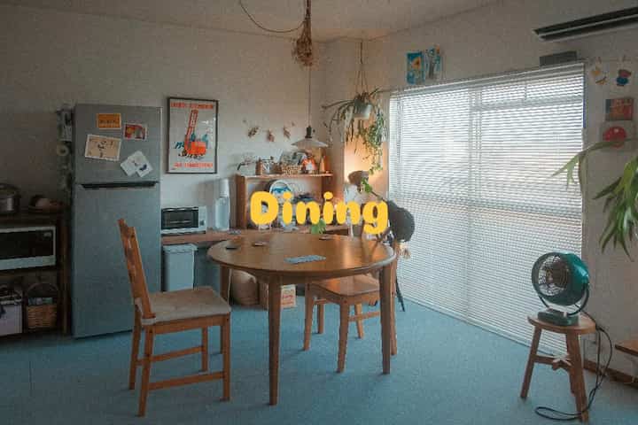 ナチュラルな色調のワンルームダイニング、木製の丸テーブルと椅子、スツールが配置された雰囲気のあるインテリア