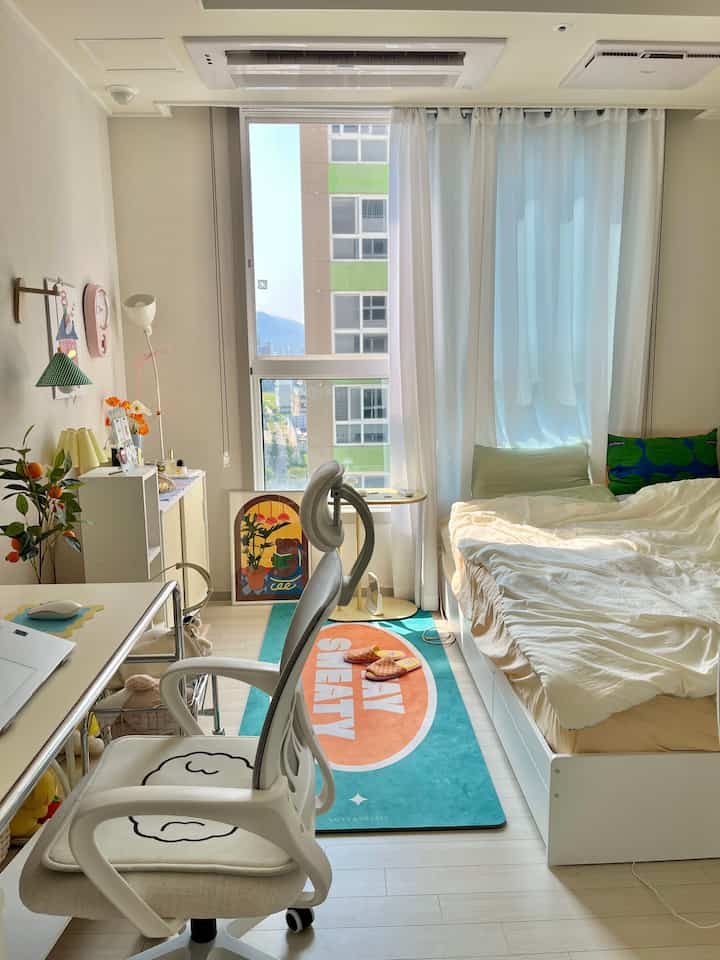 Bright square studio apartment in white tones featuring desk and bed arranged neatly