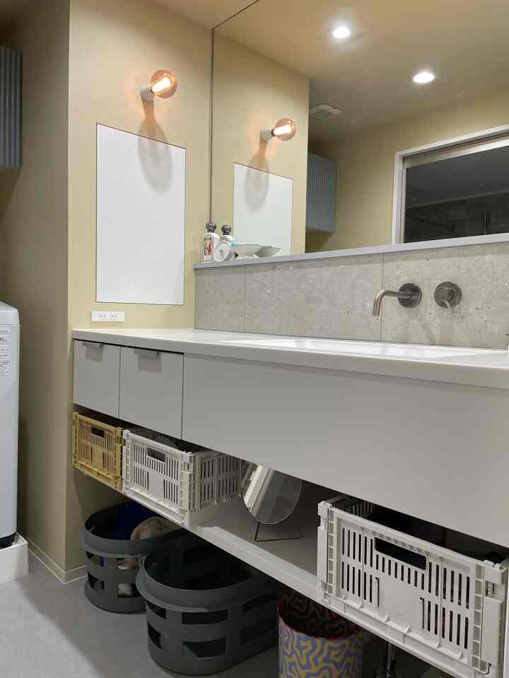 A bathroom space with beige-toned walls and a white washbasin, featuring neatly arranged baskets under the washbasin