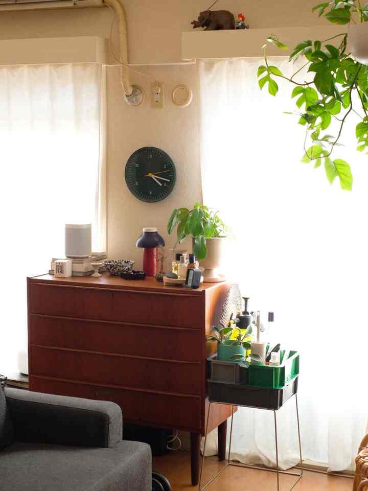 ナチュラルな色合いのリビング、ミッドセンチュリーモダンの家具が配置され、植物と壁時計が飾られた雰囲気のあるインテリア