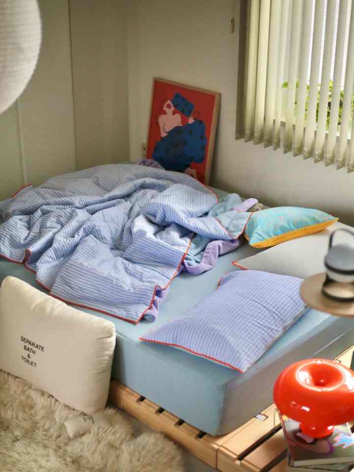 パステルブルーと木目調のワンルーム寝室、無造作に置かれた寝具が印象的な空間