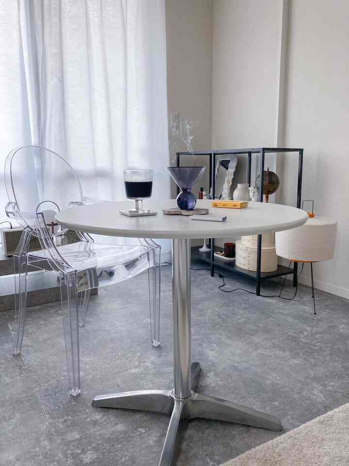 白とモノトーンの一人暮らしリビング、透明なアームチェアと円形ダイニングテーブルが配置されたシンプルな空間