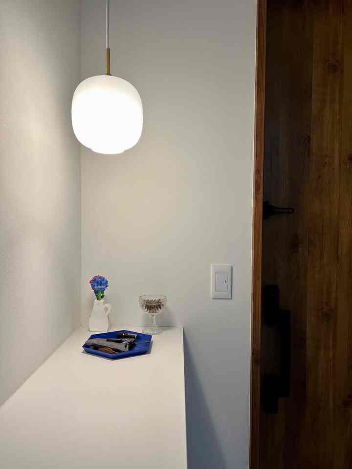 Simple white-toned entrance featuring a Louis Poulsen Radio House pendant light and a blue tray arranged neatly