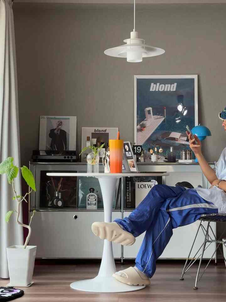 グレーの壁とホワイトのテーブルが置かれたライトブラウンの床のシンプルなワンルーム、ペンダントライトとターンテーブルが配置された空間