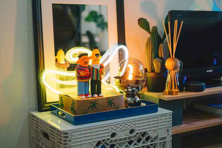 黄色のネオンサインとミッドセンチュリーモダンな小物が置かれた居心地の良いリビング、テーブルランプと植物が配置された空間