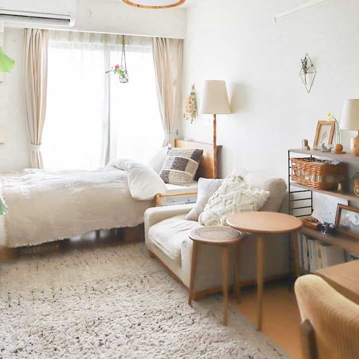 Natural tone studio apartment featuring beige sofa and bed, complemented by floor lamp and rug creating cozy atmosphere