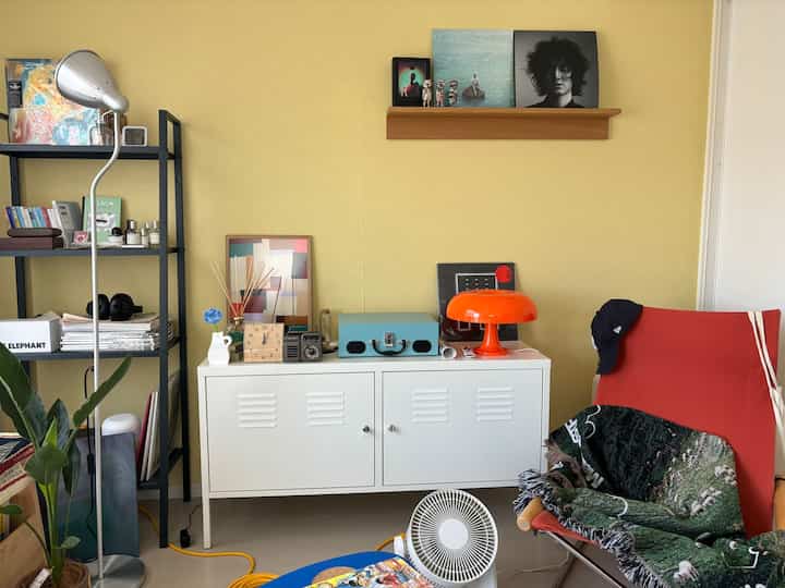 明るい黄色い壁と白いキャビネット、オレンジ色のランプと赤いアームチェアが配置された7畳のリビングルーム