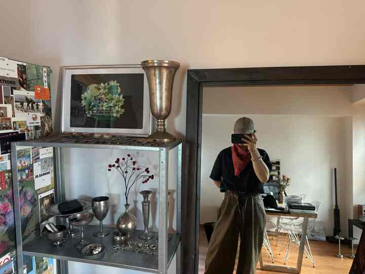 ナチュラルカラーのコンパクトなワンルーム、鉄製の棚、大きな鏡、ポスターが配置された居心地の良い一人暮らしの空間