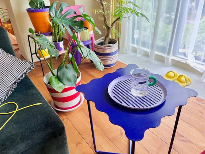 Natural color and green toned living room with sofa, blue coffee table holding a tray, and multiple potted plants creating a cozy atmosphere