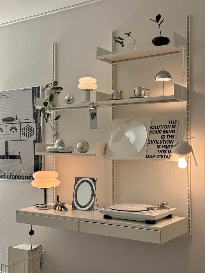 ホワイトトーンの壁に取り付けられたシステム棚とデスク、ターンテーブルやシルバーの装飾があるミッドセンチュリーモダンスタイルの空間