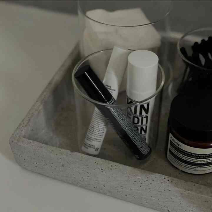 White and gray toned powder room tray featuring transparent containers and organized skincare products in a minimal setting