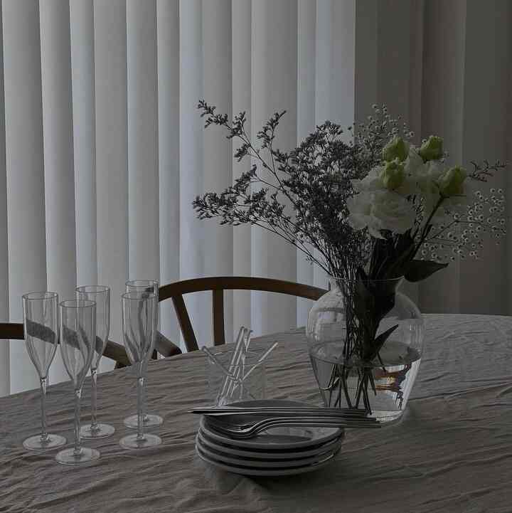 ナチュラルな色調のダイニングルーム、木製のダイニングチェアと花瓶が置かれたテーブルウェアのある落ち着いたインテリア