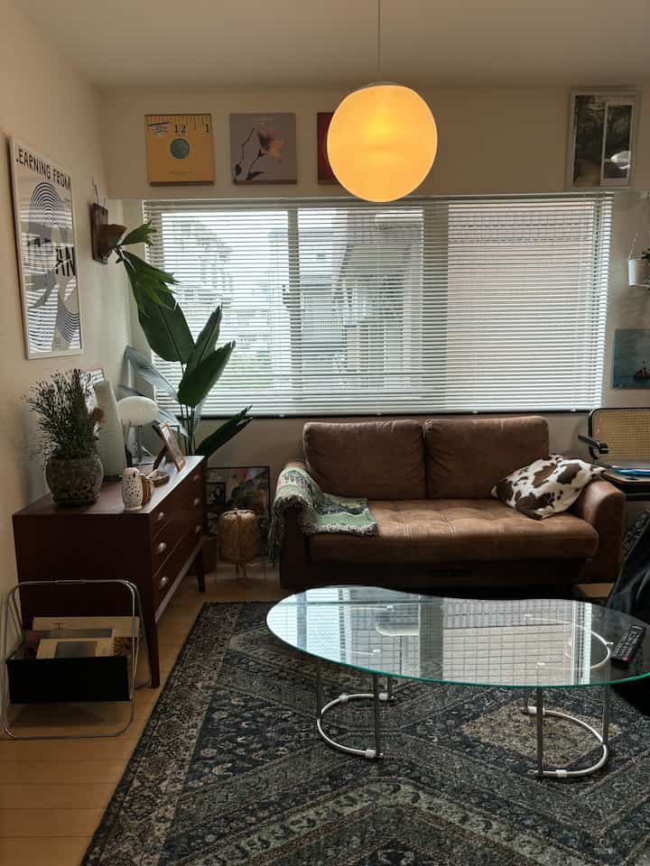 Natural-toned living room with brown sofa and glass coffee table, featuring a round pendant light creating a warm ambiance