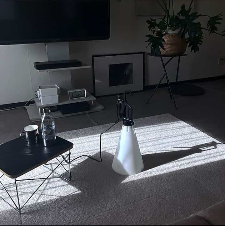 明るい陽射しが差し込むシンプルなリビング、中央にflos maydayのテーブルランプと白いカーペット、ワイヤーベースのローテーブルが配置された空間