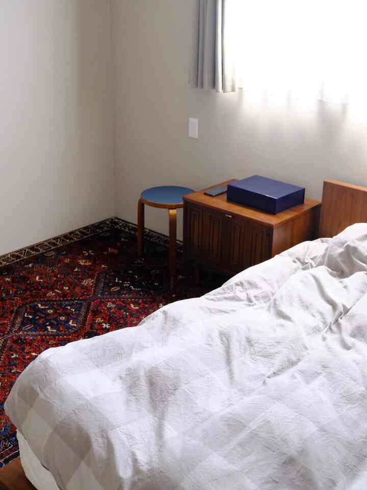 白と木目調を基調とした寝室、赤いカーペットと青いスツールが配置された温かみのある空間