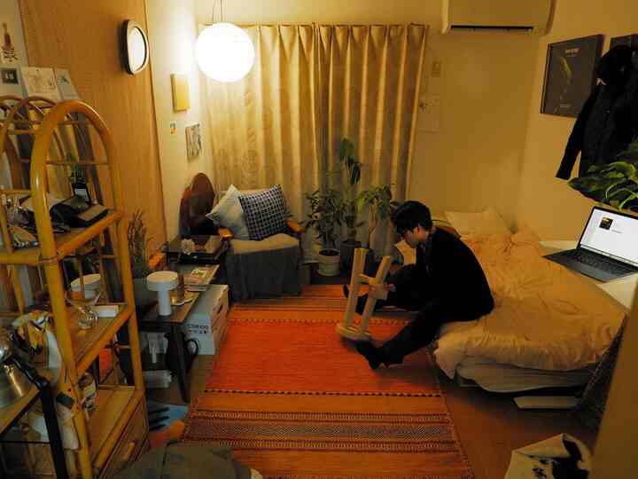 Beige and orange tone studio apartment living room featuring armchair, plants, and bed in a cozy compact space