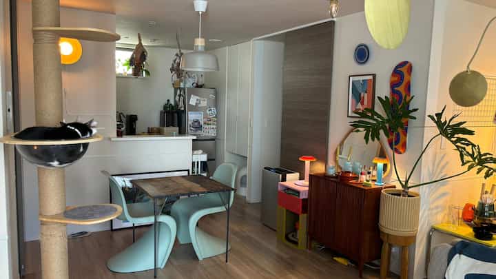 White-walled and wood-toned two-person dining room featuring a cat tower and plants, creating a cozy modern space