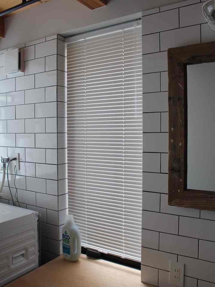 Clean laundry room featuring a vertical window with white aluminum blinds, white tiled walls, and a washing machine