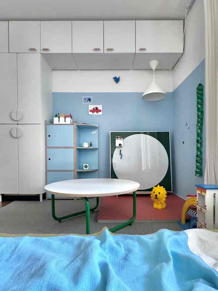 白と青の色調の子供部屋、丸い遊び用テーブルとおもちゃ収納が配置された整然とした居心地の良い空間