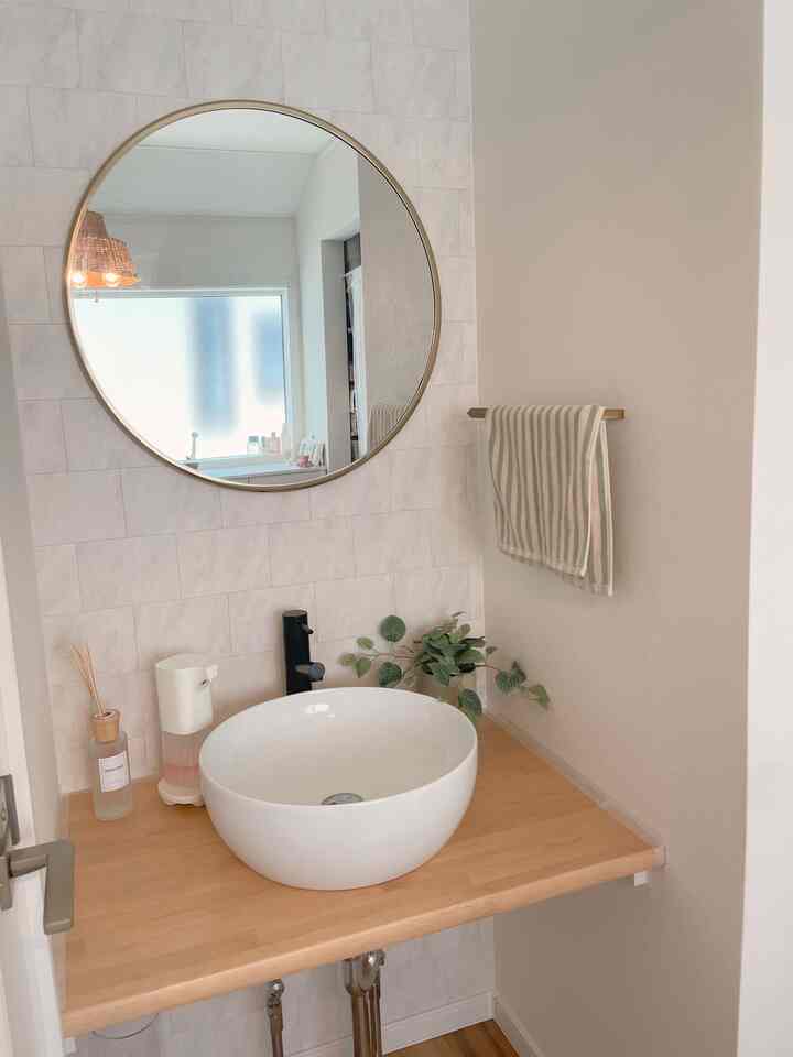 白と木目調が調和したホテルライクなバスルーム、丸い鏡と清潔感のある洗面台が配置された印象的な空間