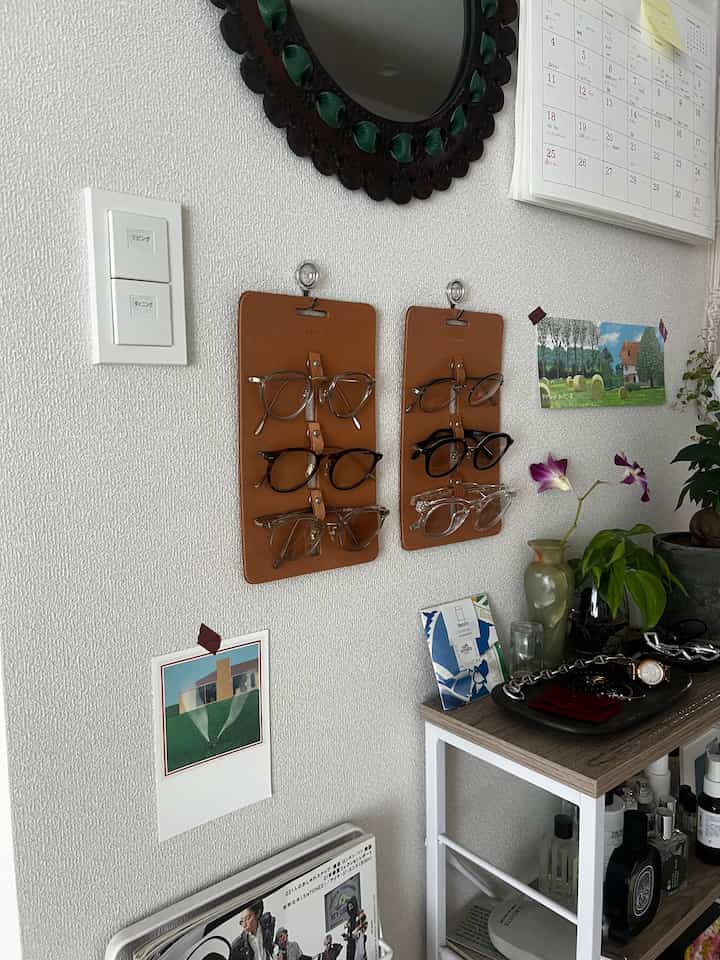 白い壁にレザー製のメガネホルダーが掛けられ、右側には植物と小物が置かれたナチュラルトーンのコンソールテーブルが配置された居心地の良い北欧風リビング空間