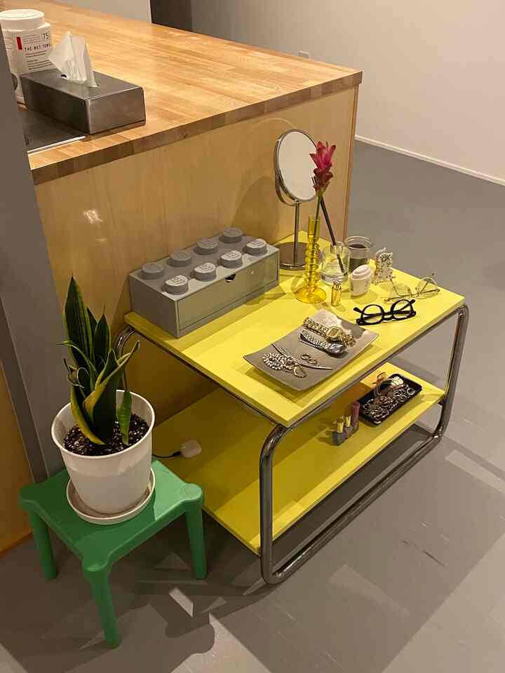 明るい黄色のサイドテーブルと木目調のカウンター、隣に白い鉢と緑の植物が配置されたシンプルで落ち着いた空間