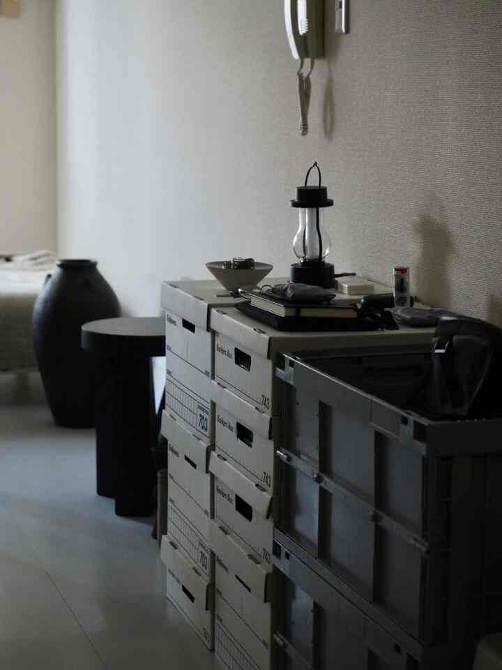 ベージュ色調の狭い部屋、バンカーズボックスとプラスチック収納箱が置かれたモダンな収納空間