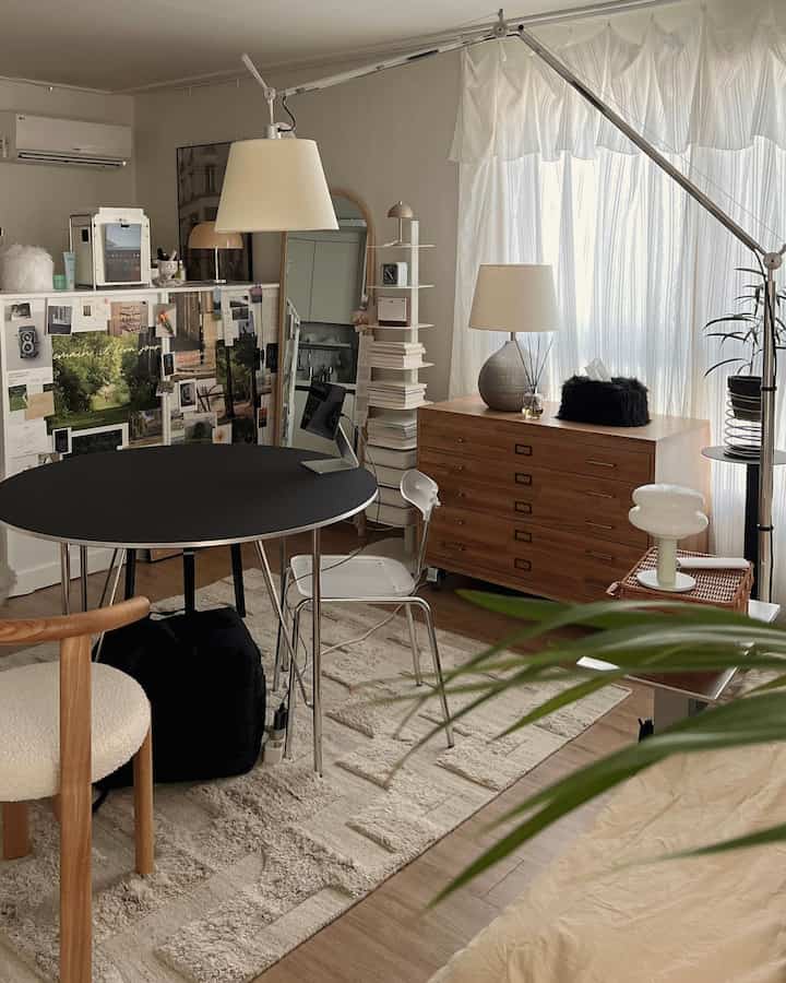 ナチュラルな木目調と黒いテーブルがある8畳のワンルーム、カーテンとラグが配置された温かみのあるインテリア