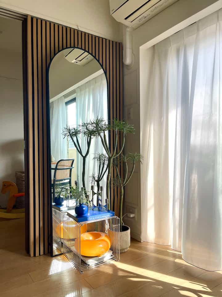 Bright modern entrance space featuring warm wood tone wall panel with large arched mirror, plants, and metal side table