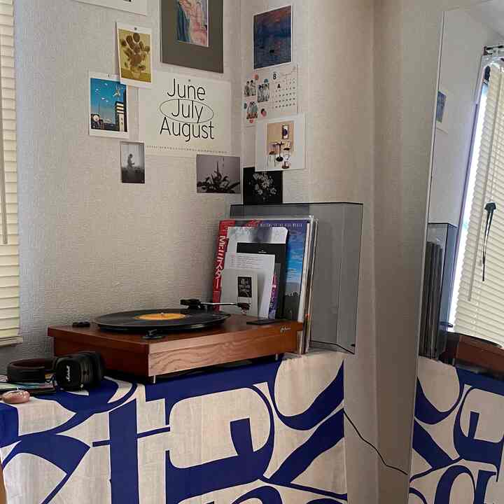 白い壁と青いファブリックが調和するコーナーに木目調のレコードプレーヤーが配置されたヴィンテージ感のあるインテリア