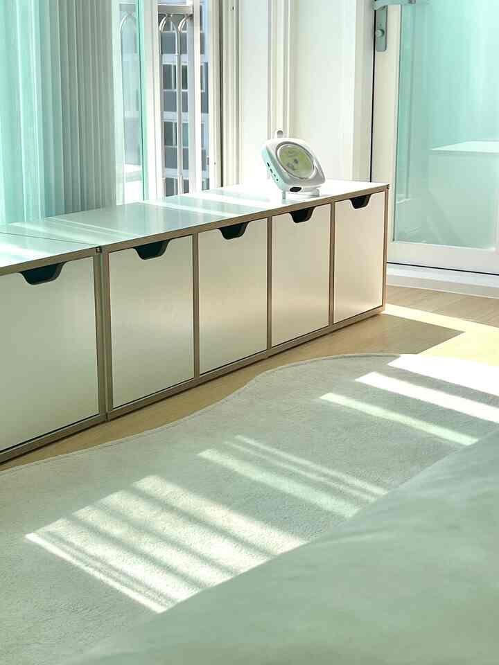 明るくナチュラルな色調の子供部屋、窓際に配置された白いベンチ収納とベージュの木製床、明るいカーテンがある雰囲気のあるインテリア