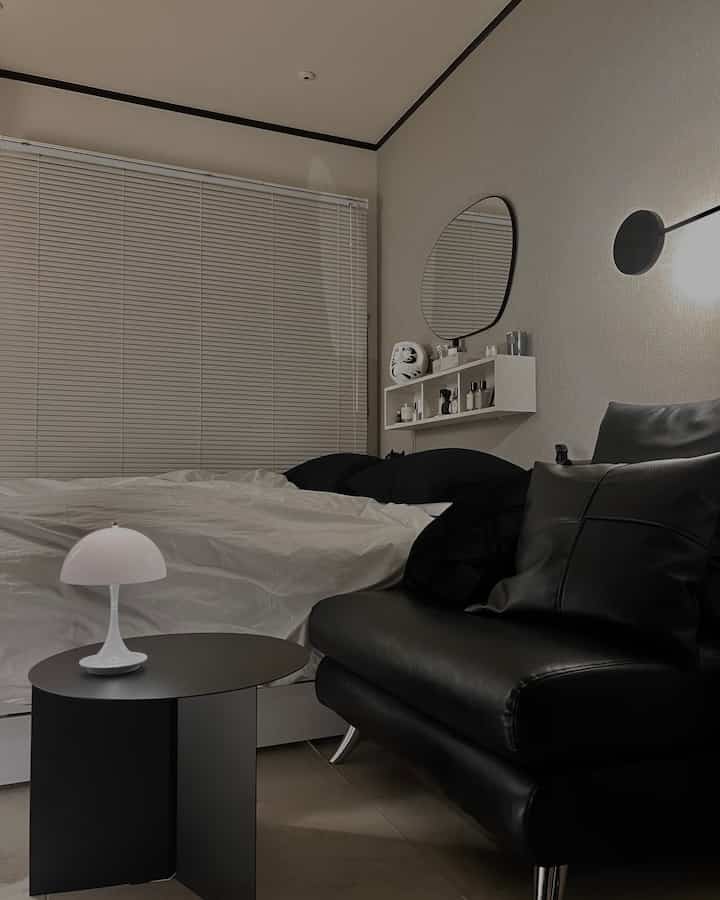 白と黒のトーンの狭い寝室、黒のレザーアームチェアと白いベッドが配置されたモダンでナチュラルな雰囲気のインテリア