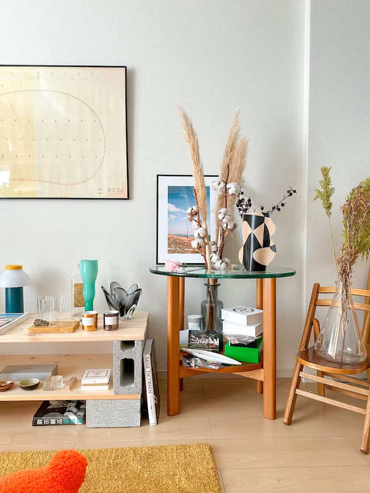 ナチュラルカラーのリビングの一角、木製のサイドテーブルと多様な花瓶やオブジェが配置された雰囲気のある空間