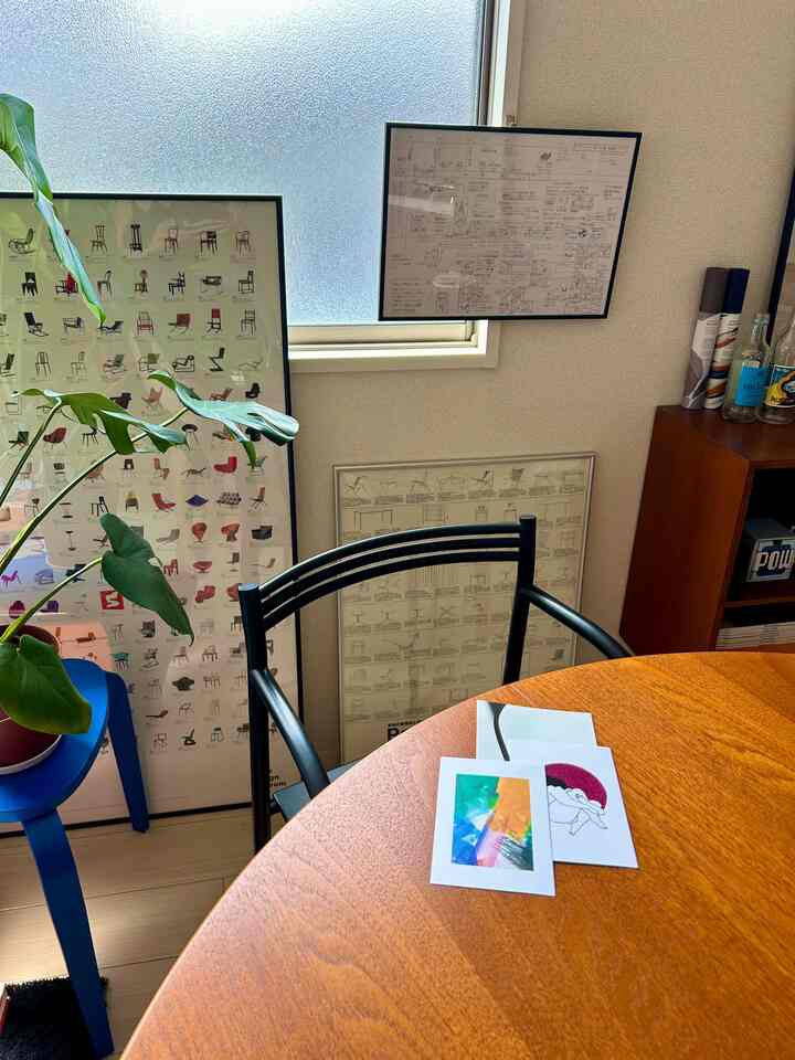 白い壁と木目調のテーブルがあるミッドセンチュリーモダンのダイニング、ポスターと植物が配置された雰囲気のある空間